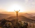 Man standing on hill with arms up facing sunset