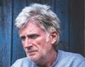 Middle aged man sitting in front of a blue wooden door