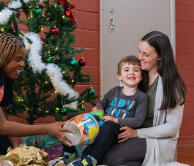 A mother being gioven a christmas gift by a salvos volunteer with her son 