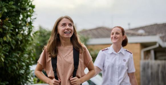 Ava smiling carrying her school backpack with a Salvos personnel next to her