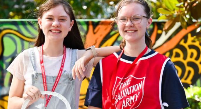 Two young Red Shield Volunteers collect with bucket and Tap-n-go unit